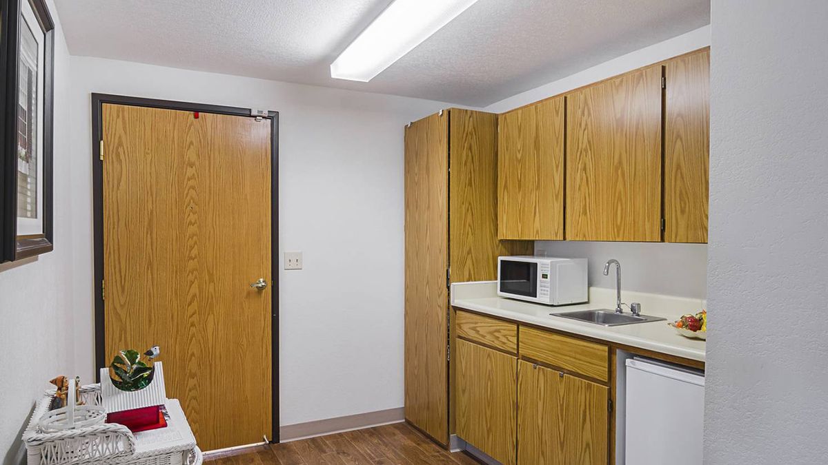 A small kitchenette with wooden cabinets, a microwave, and a sink.