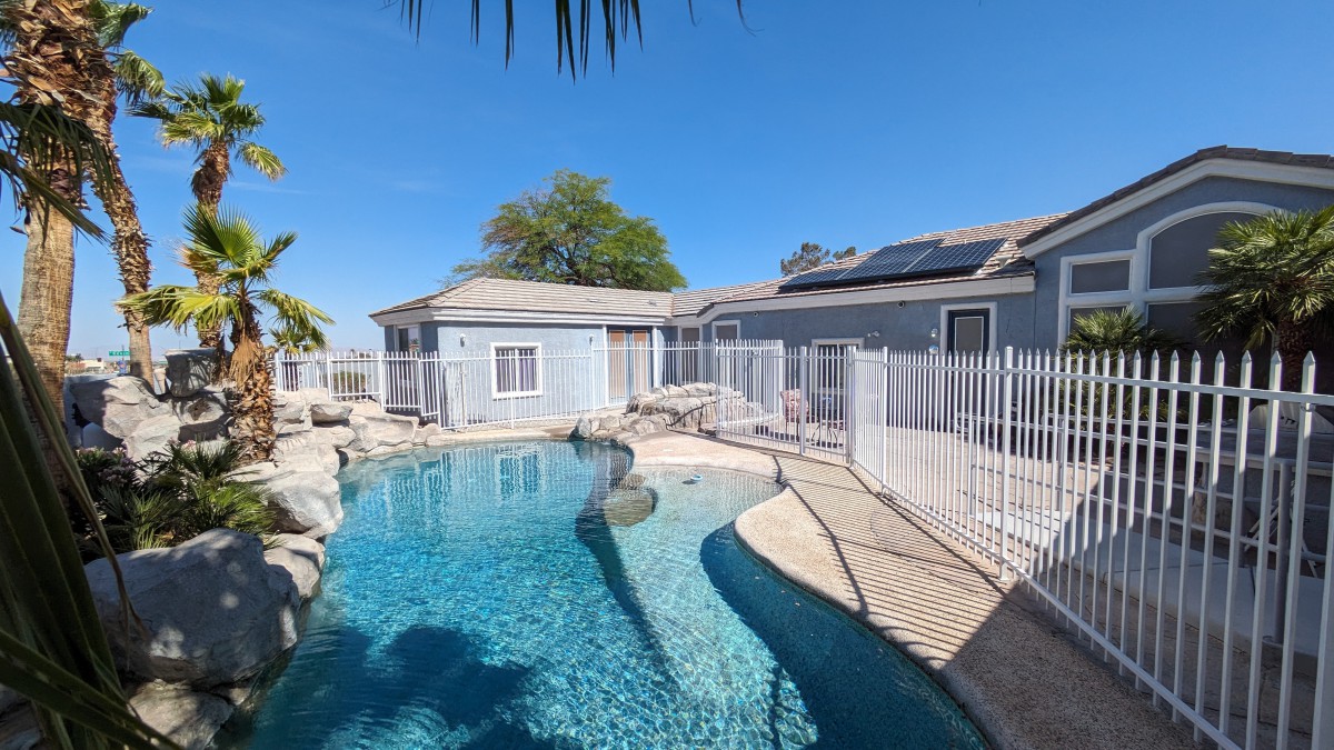 A residential backyard featuring a swimming pool and a fenced area under a clear blue sky.