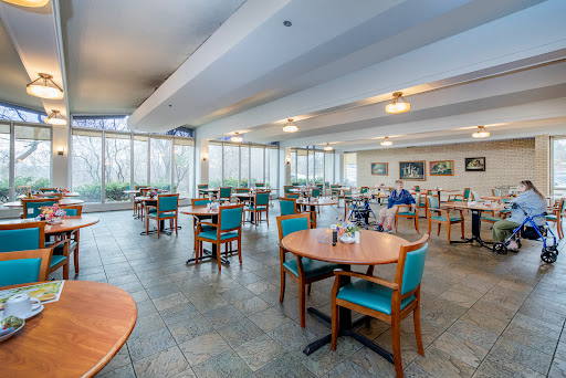 A spacious and modern dining area featuring wooden tables and teal chairs, illuminated by natural light.
