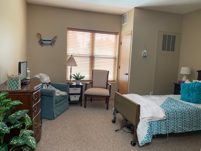 A cozy bedroom with a bed, chairs, and a window letting in natural light.