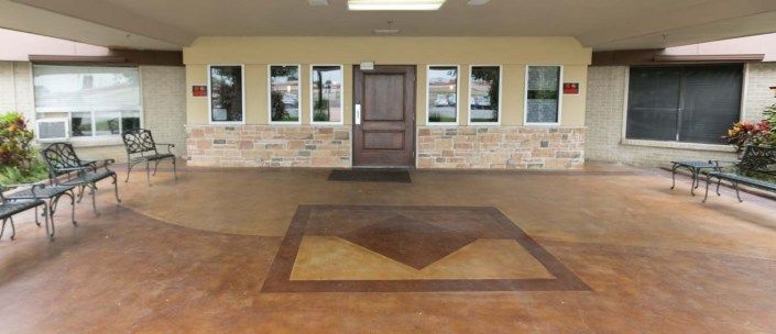 The image shows a building entrance with a wooden door, surrounded by windows and a decorative brick wall, accompanied by a patterned concrete floor.