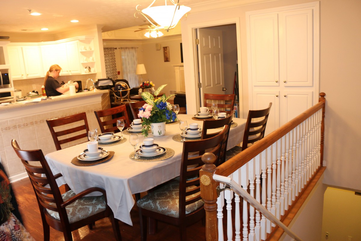 A warmly lit dining room with a set table and adjacent open kitchen area.