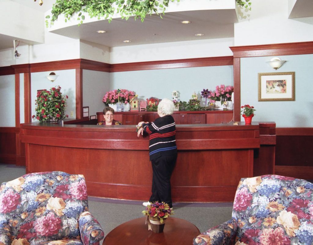 A woman standing at a reception desk in a lobby with floral decorations.