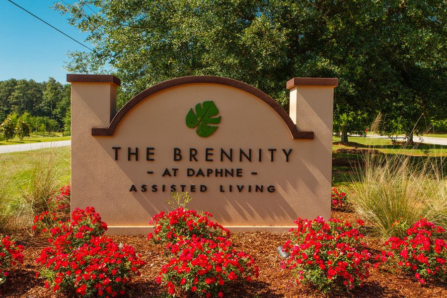 The Brennity at Daphne Assisted Living sign surrounded by red flowers and trees.