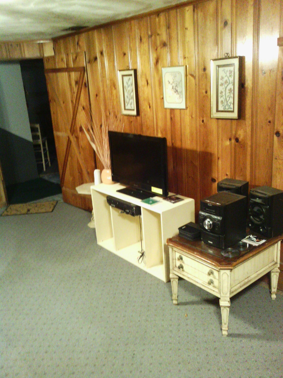 A cozy living room with wood-paneled walls, featuring a television and stereo system on wooden furniture.