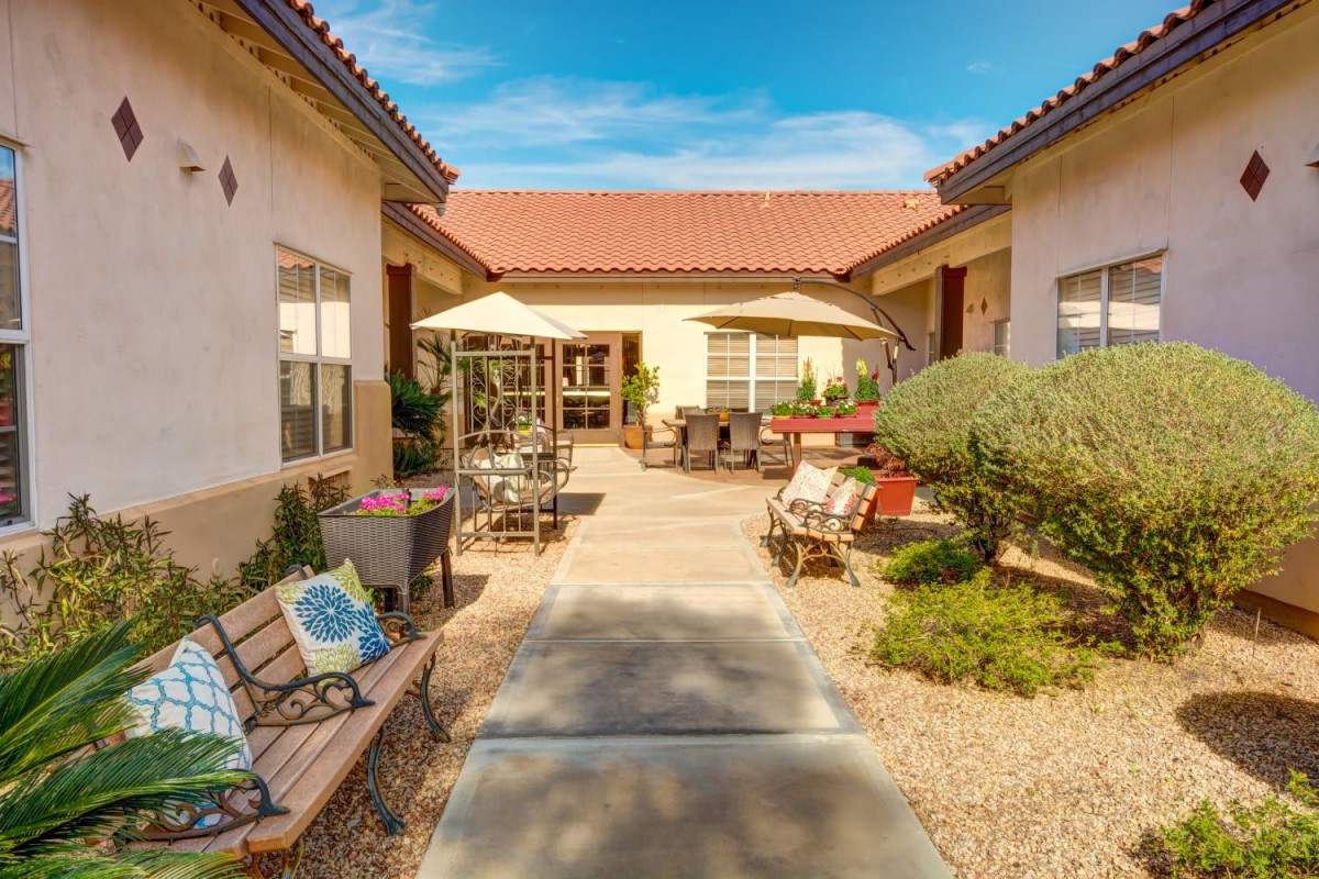 A sunny courtyard featuring benches, umbrellas, and desert landscaping.