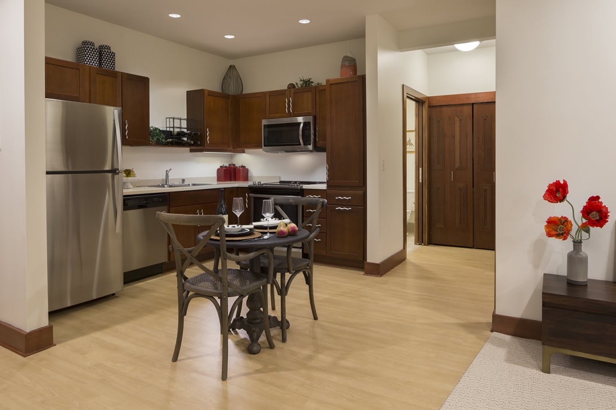 A modern kitchen with wooden cabinets, stainless steel appliances, and a dining table set.