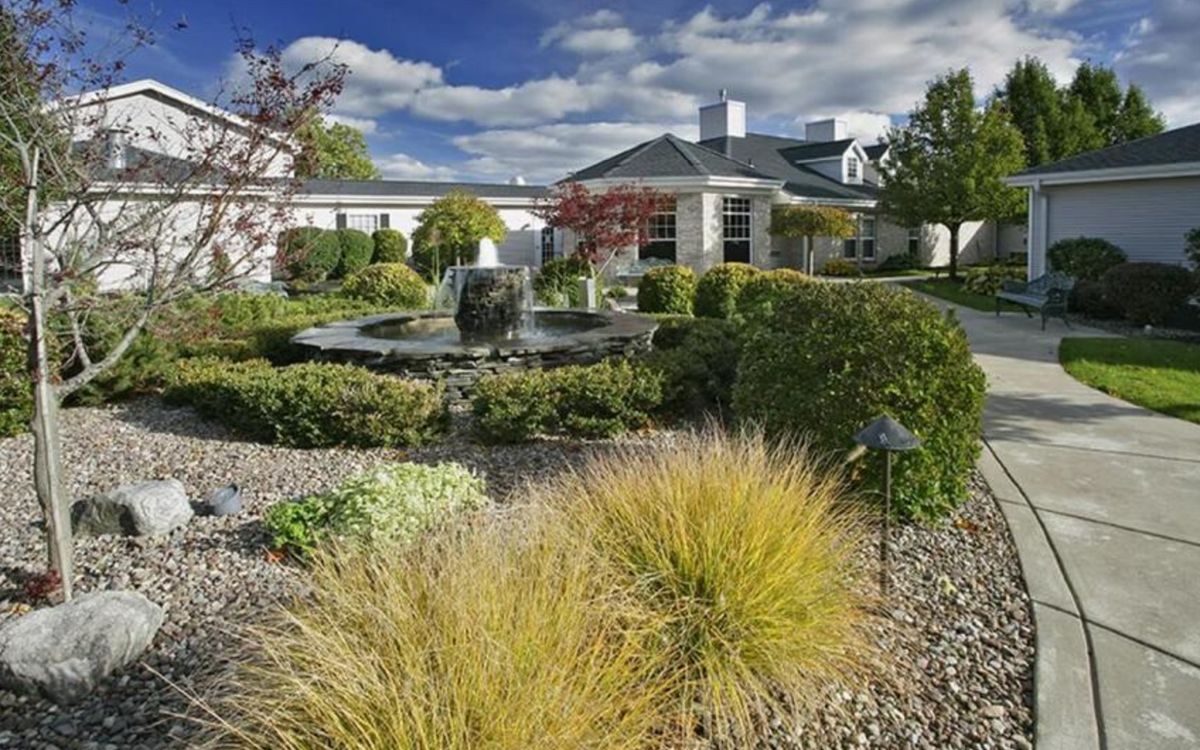 A scenic view of a landscaped garden with a central fountain, surrounded by a modern building and clear blue sky.