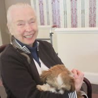 A smiling woman holding a small dog indoors.