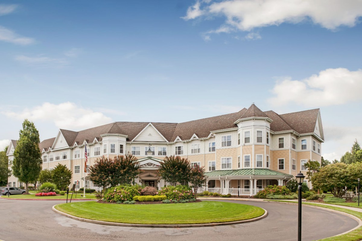A large residential building with a roundabout and well-maintained landscaping under a clear blue sky.