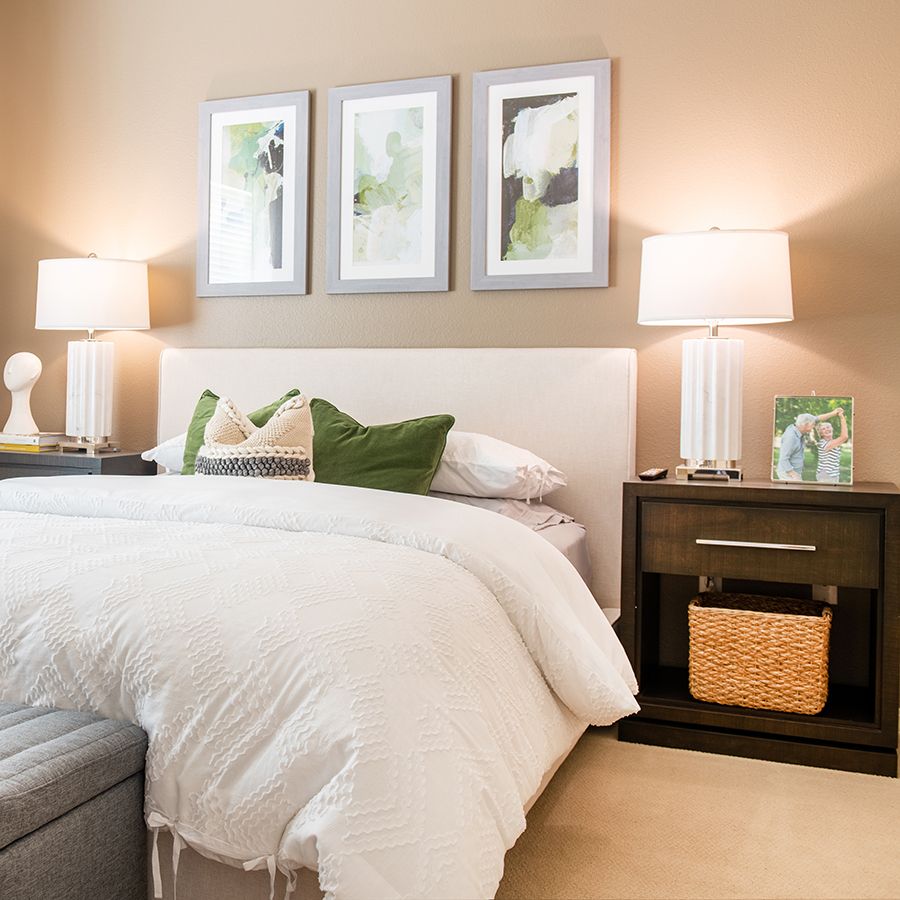 A cozy bedroom with elegant decor, featuring a bed with white bedding, two side tables with lamps, and three framed pictures on the wall.