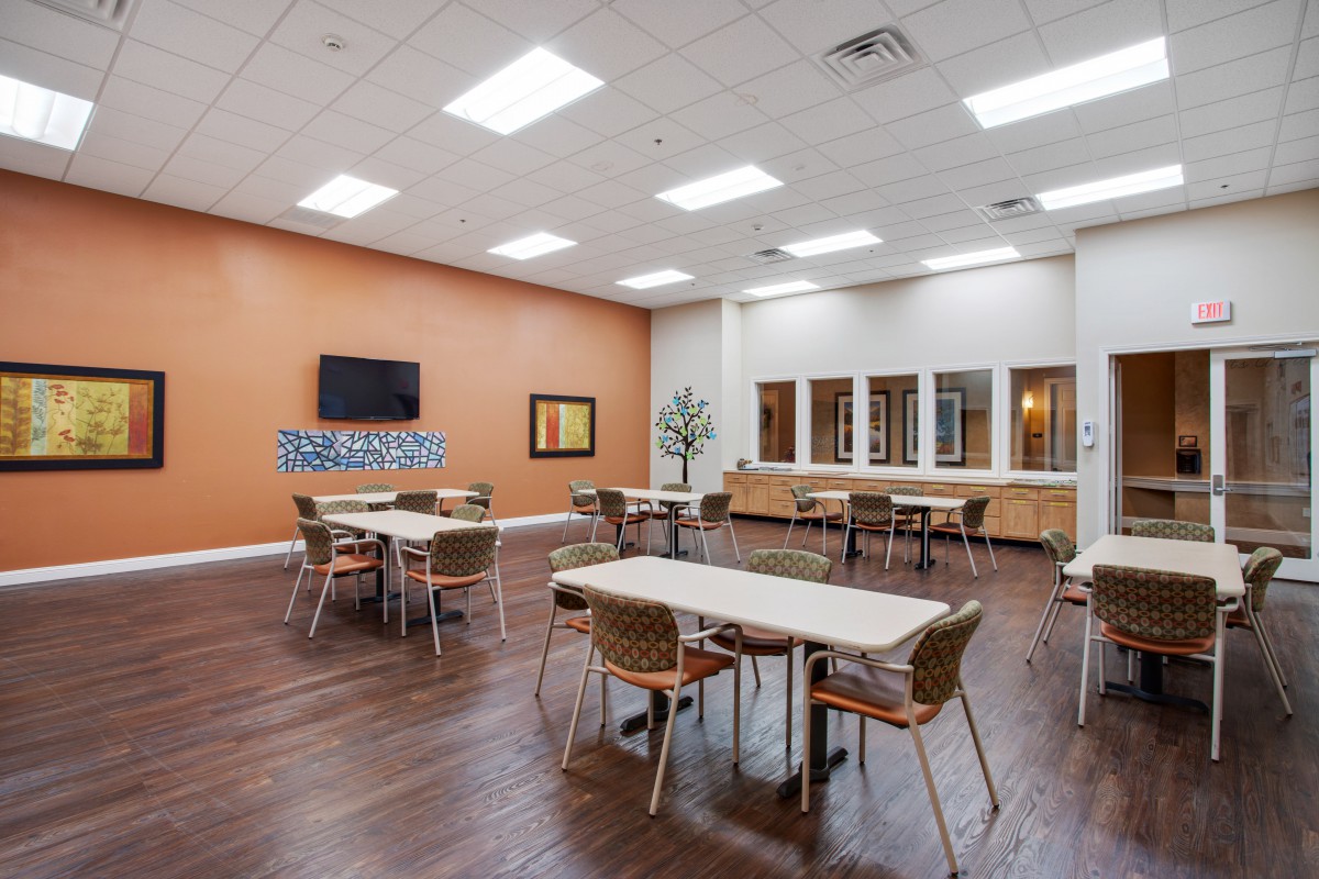 A modern dining area with tables and chairs, featuring hardwood floors and a television on the wall.