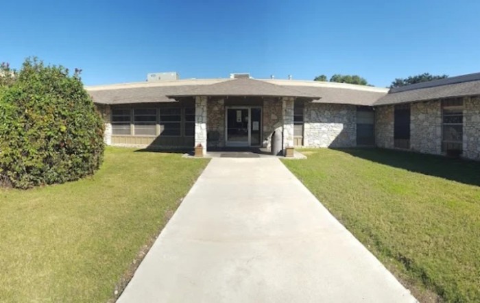 A front view of a building with a concrete sidewalk leading to the entrance under a clear blue sky.