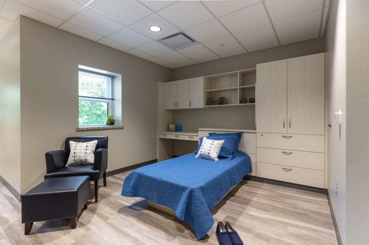 A modern and minimalist single bedroom with blue bedding, featuring built-in storage and natural lighting.