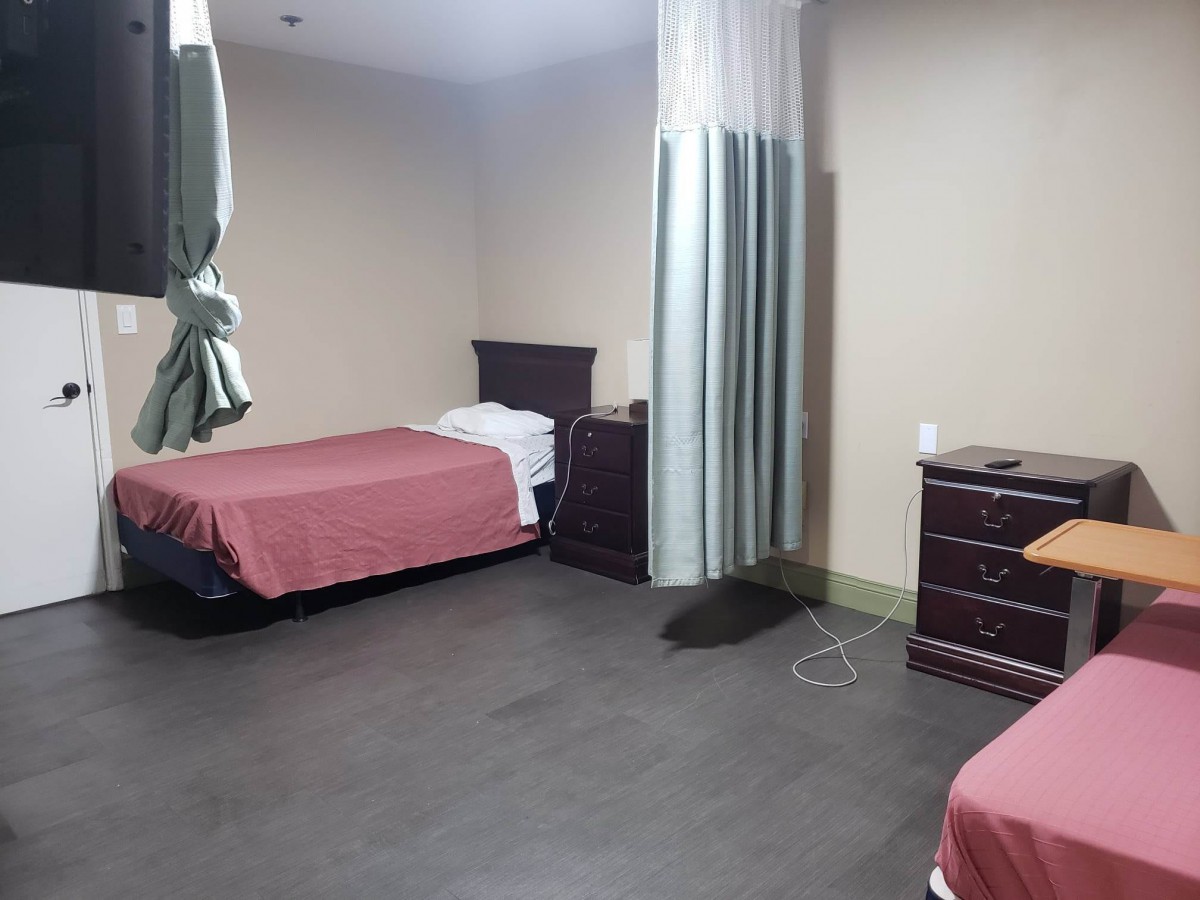 A hospital room with two beds, separated by a privacy curtain, featuring minimalist decor and wooden furniture.