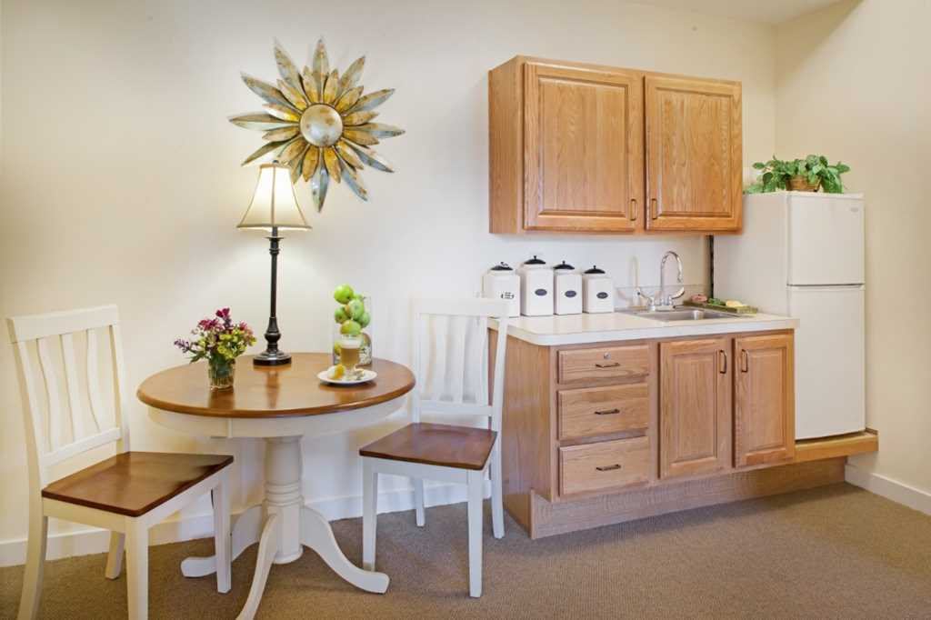 A cozy kitchen corner with a small round dining table and chairs, complemented by wooden cabinets and decorative items.
