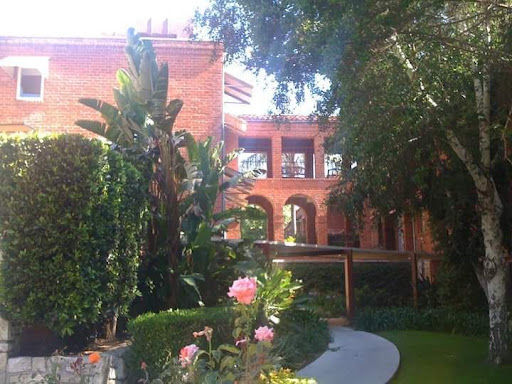 A beautiful view of a brick building surrounded by lush greenery and blooming flowers.