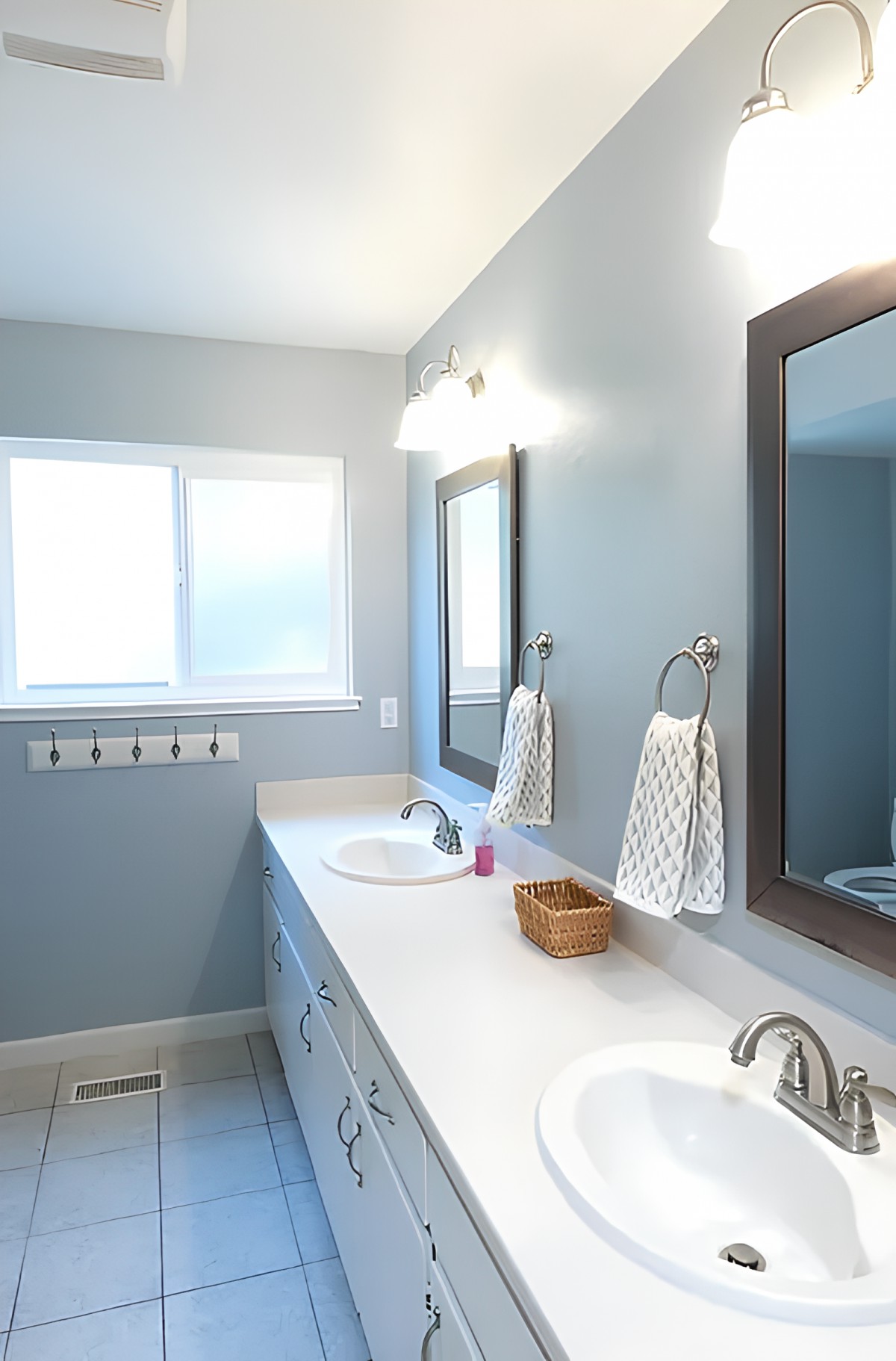 A modern bathroom with dual sinks, mirrors, and a window illuminating the space.