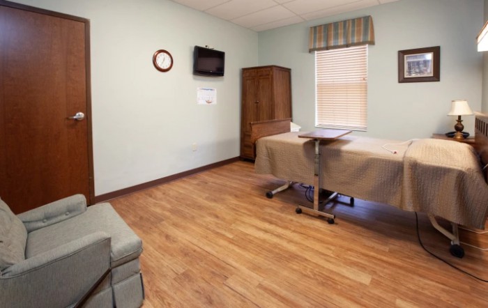 A hospital room with a bed, TV, and clock on the wall.