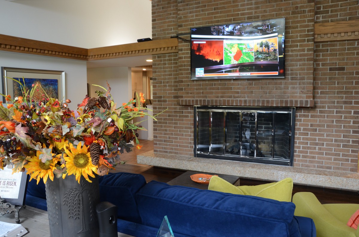 A cozy living room with a brick fireplace and television above, featuring a blue sofa and a vibrant floral arrangement.