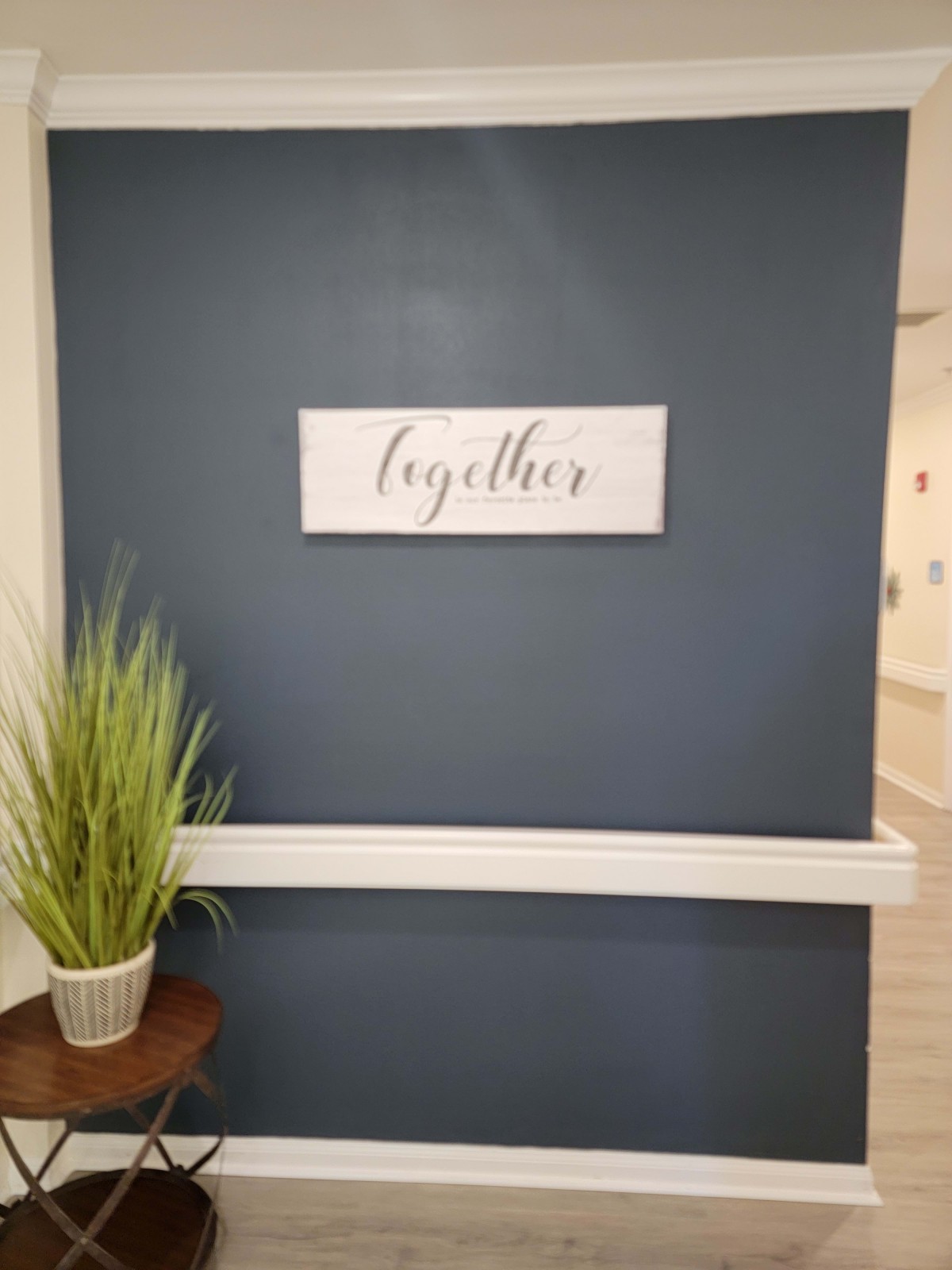 A minimalist indoor setting with a decorative sign reading 'together', complemented by a potted plant on a wooden table against a dark blue wall.