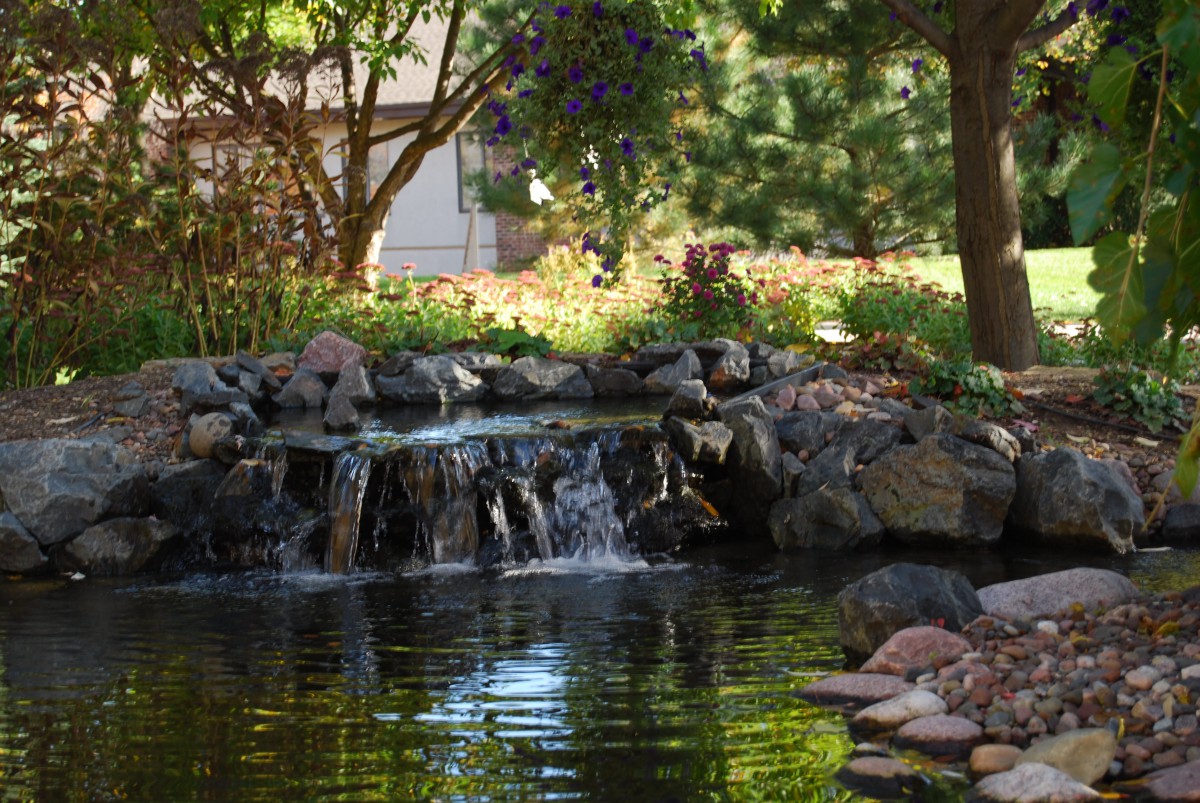 A tranquil garden pond with a small waterfall surrounded by rocks and trees.