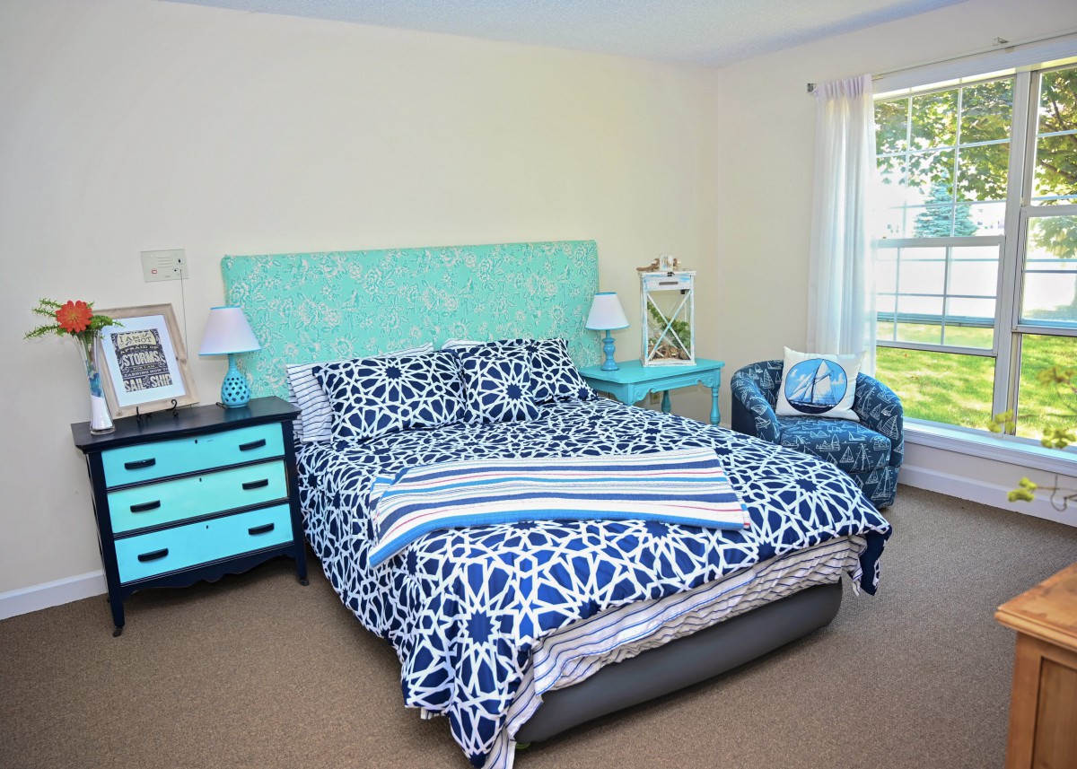 A cozy bedroom with a blue and white color scheme, featuring a bed with patterned bedding, matching furniture, and natural light streaming in through the window.