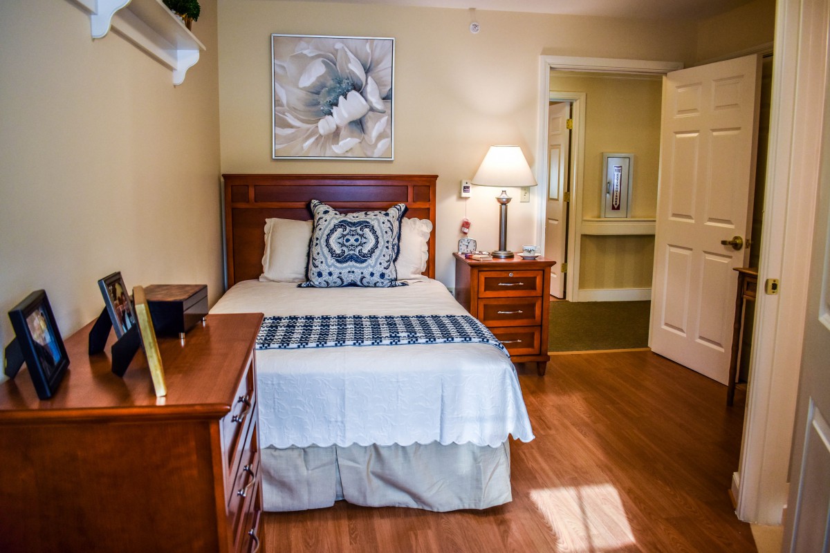 A cozy bedroom featuring a single bed with a wooden headboard, matching nightstands, and a decorative lamp on one side.