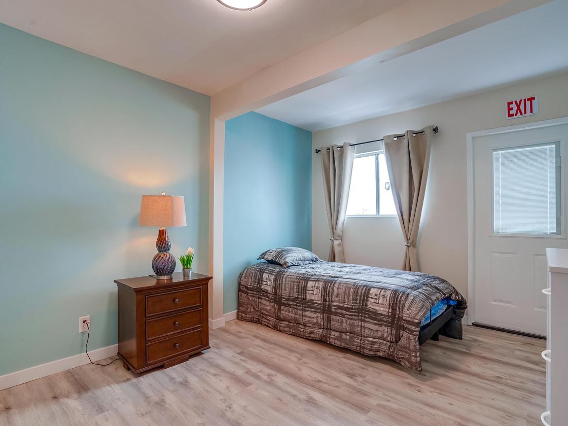 A cozy bedroom with a single bed, nightstand, and a lamp, featuring blue accent walls and hardwood flooring.