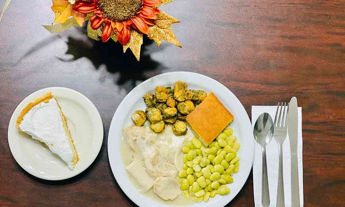 A well-balanced meal featuring mashed potatoes, brussels sprouts, cheese, and beans is served on a plate with a flower centerpiece.