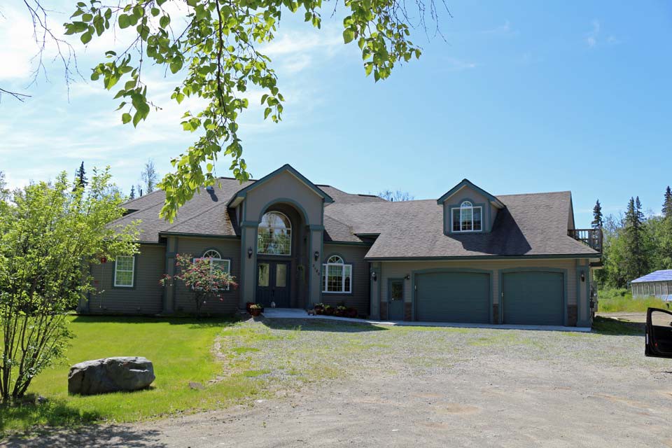 A spacious suburban house with a three-car garage, surrounded by greenery on a sunny day.