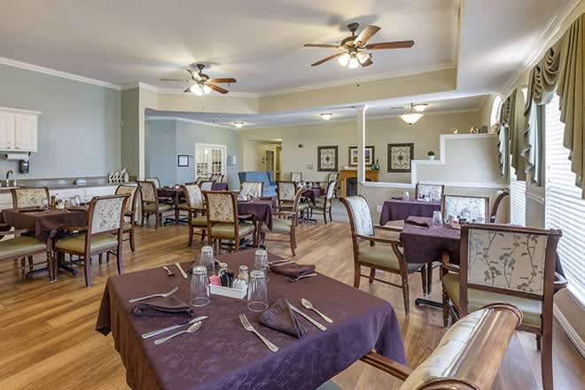 A well-lit dining room with neatly arranged tables and chairs, featuring ceiling fans and subtle decor.