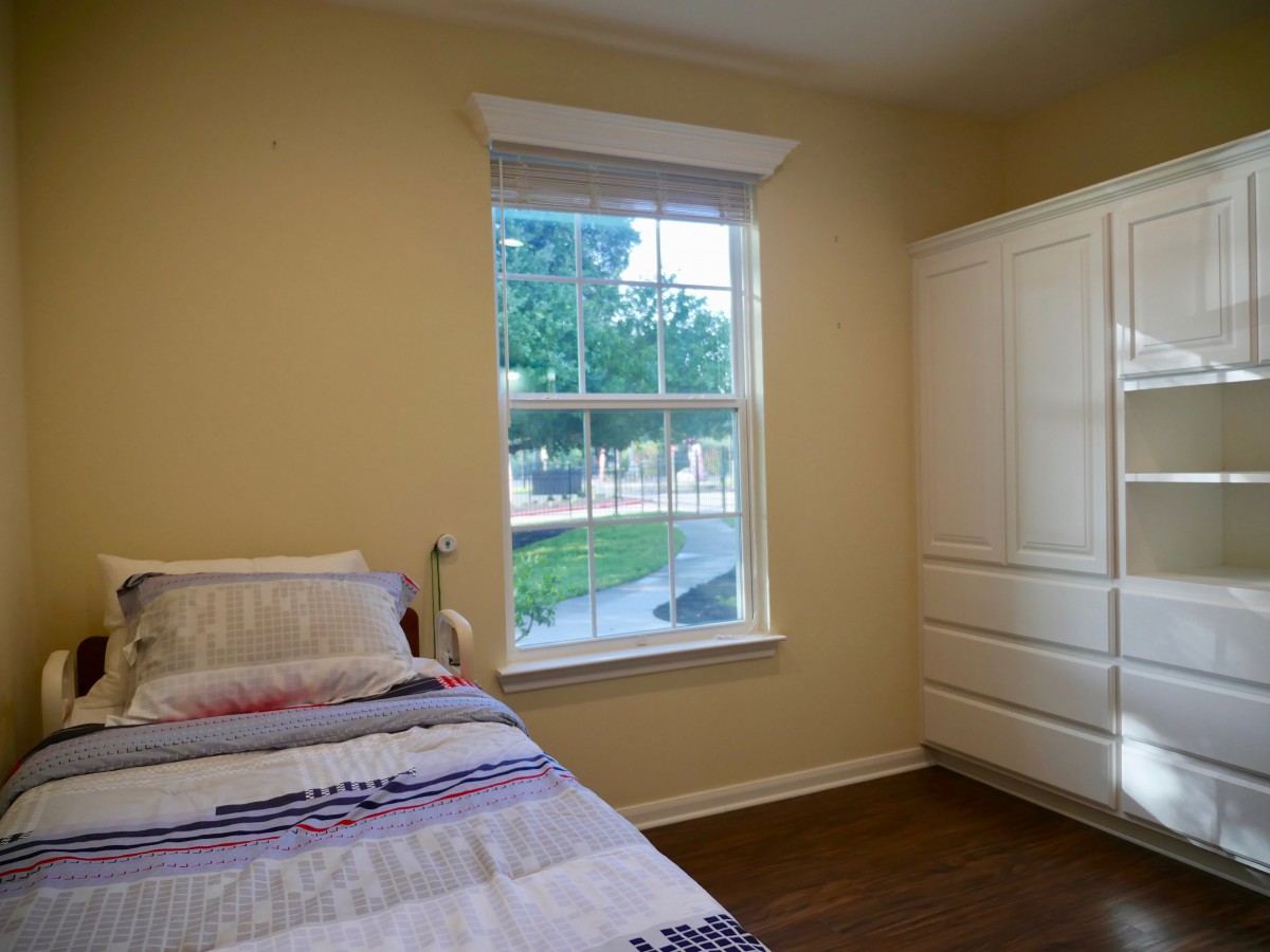A bright and simple bedroom with a single bed, window, and white wardrobe.