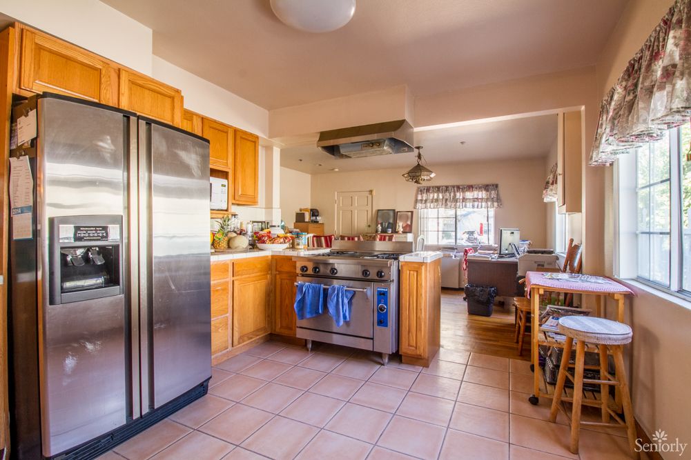 A cozy kitchen with wooden cabinets, a stainless steel refrigerator, and a stove, leading into a bright dining area.
