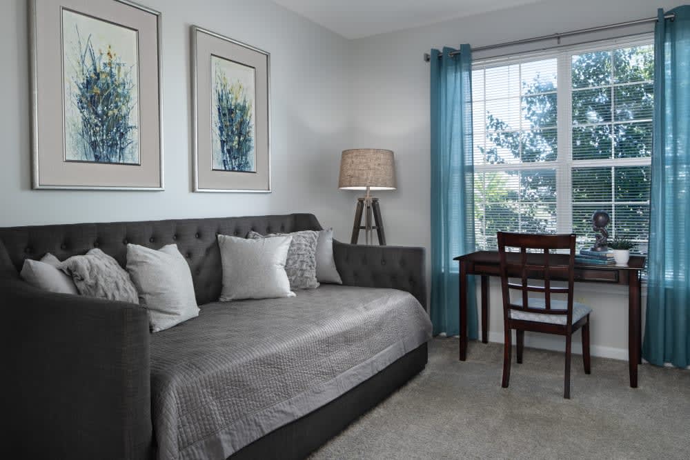 A cozy living room with a stylish sofa, desk, and floor lamp next to a large window with blue curtains.