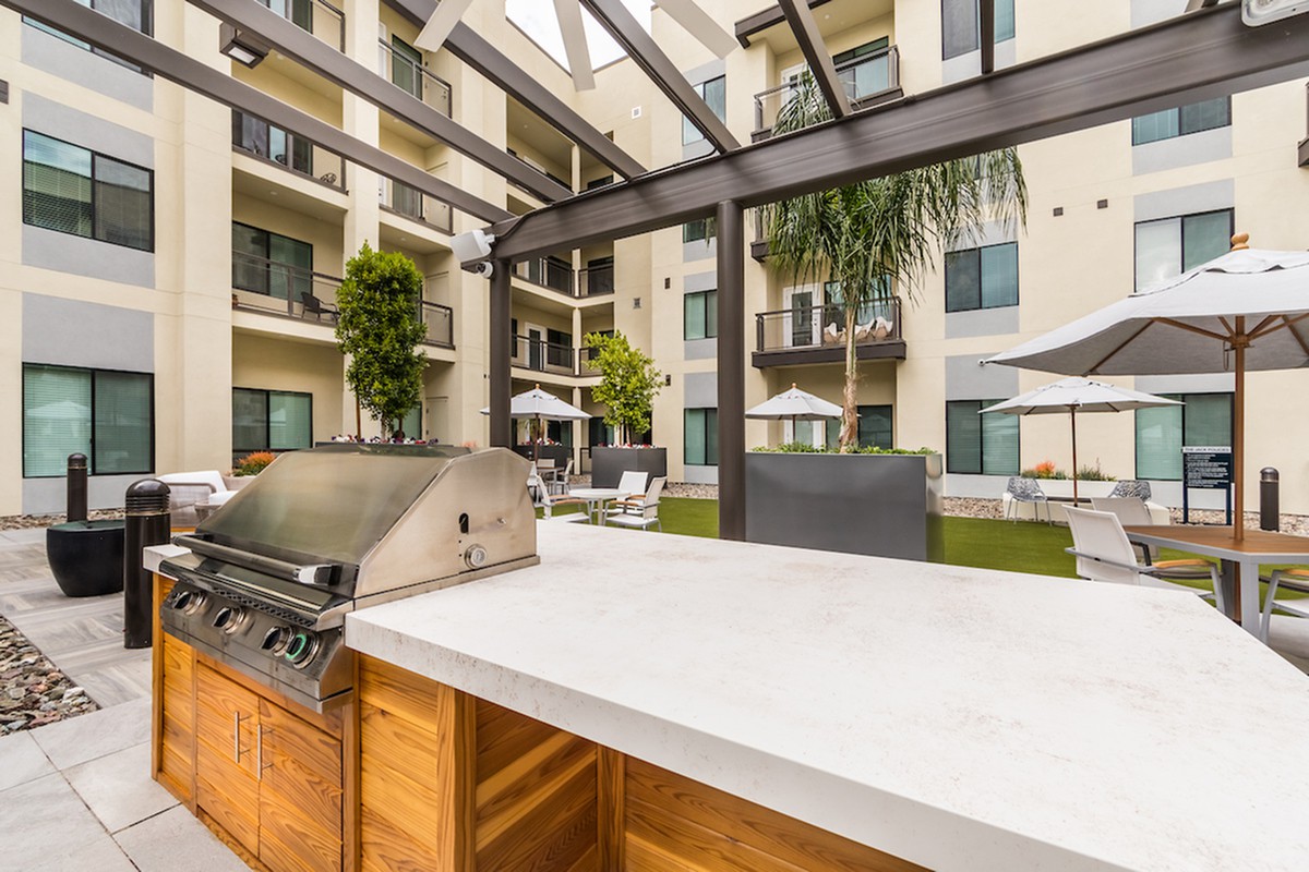 Outdoor barbecue area in an apartment complex with seating and greenery.
