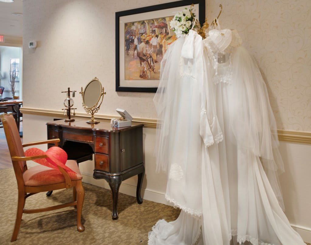 A cozy bridal room featuring a wedding dress on display beside a vanity table and mirror, adorned with elegant artwork.