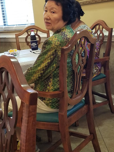 A woman sitting at a dining table, wearing vibrant attire.
