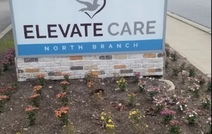 A healthcare facility sign with a flower garden in front.