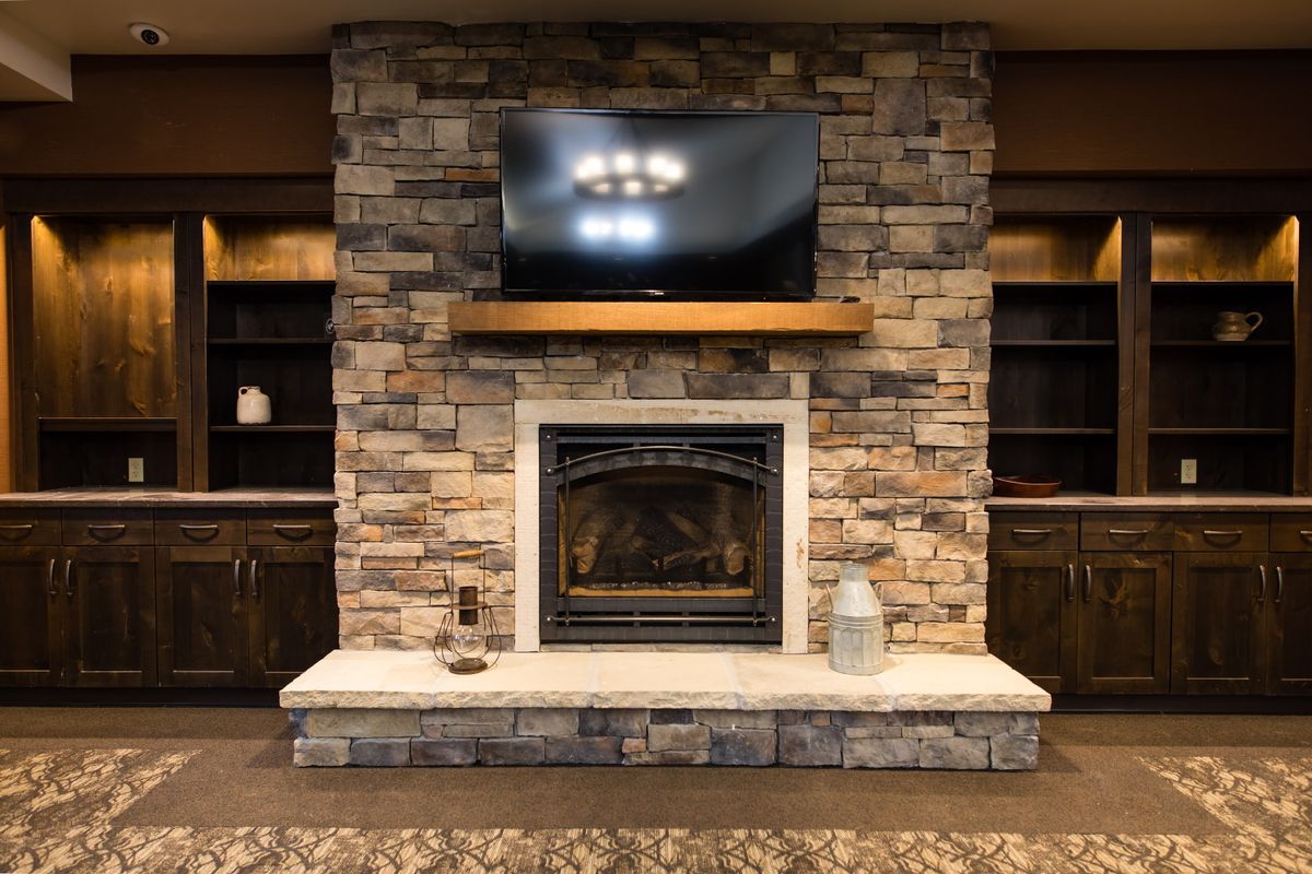 A cozy living room with a stone fireplace and a television mounted above it.