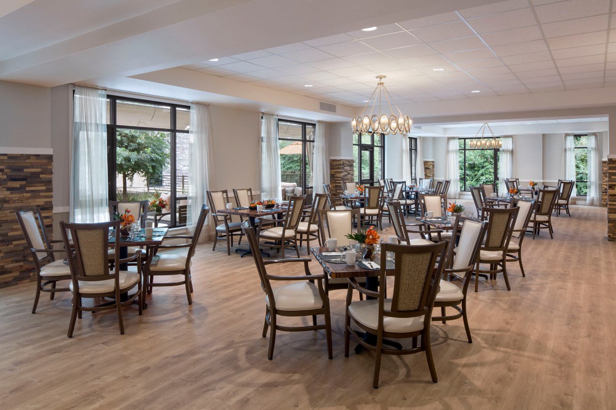 A spacious and elegantly decorated dining room with modern tables and chairs, featuring large windows and a chandelier.