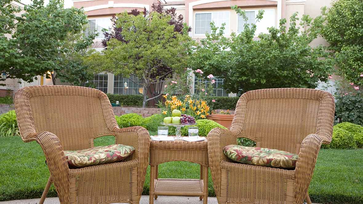 A cozy outdoor seating area with wicker chairs and a table, surrounded by lush greenery and flowers.