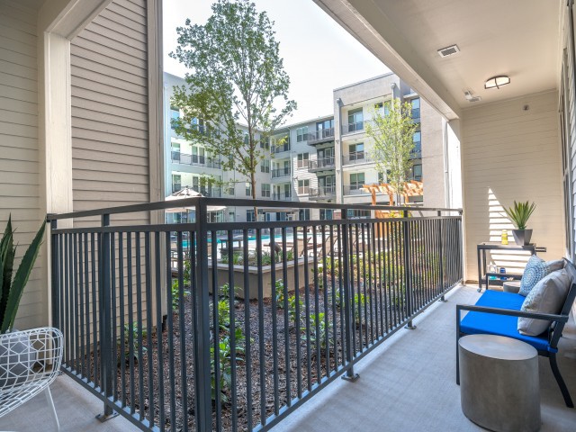 A modern apartment balcony with outdoor seating overlooking a well-maintained courtyard.