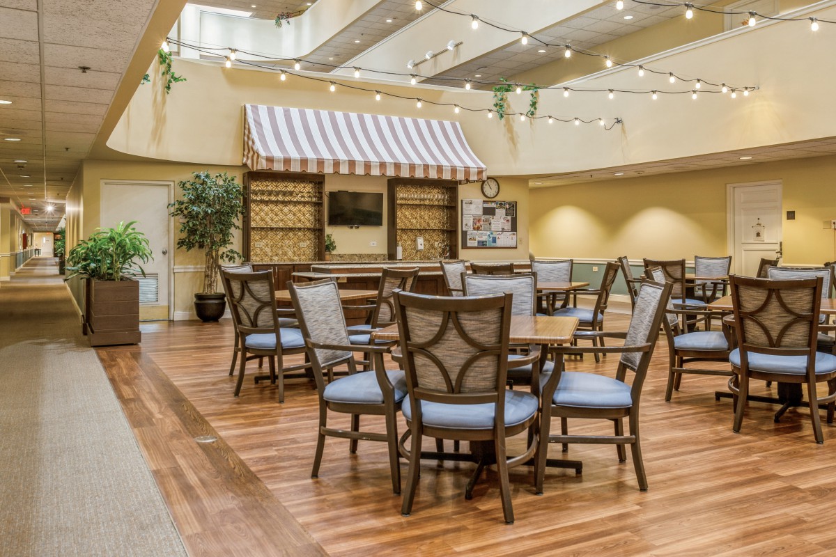 A cozy indoor social area with wooden flooring, featuring tables and chairs under decorative lighting.