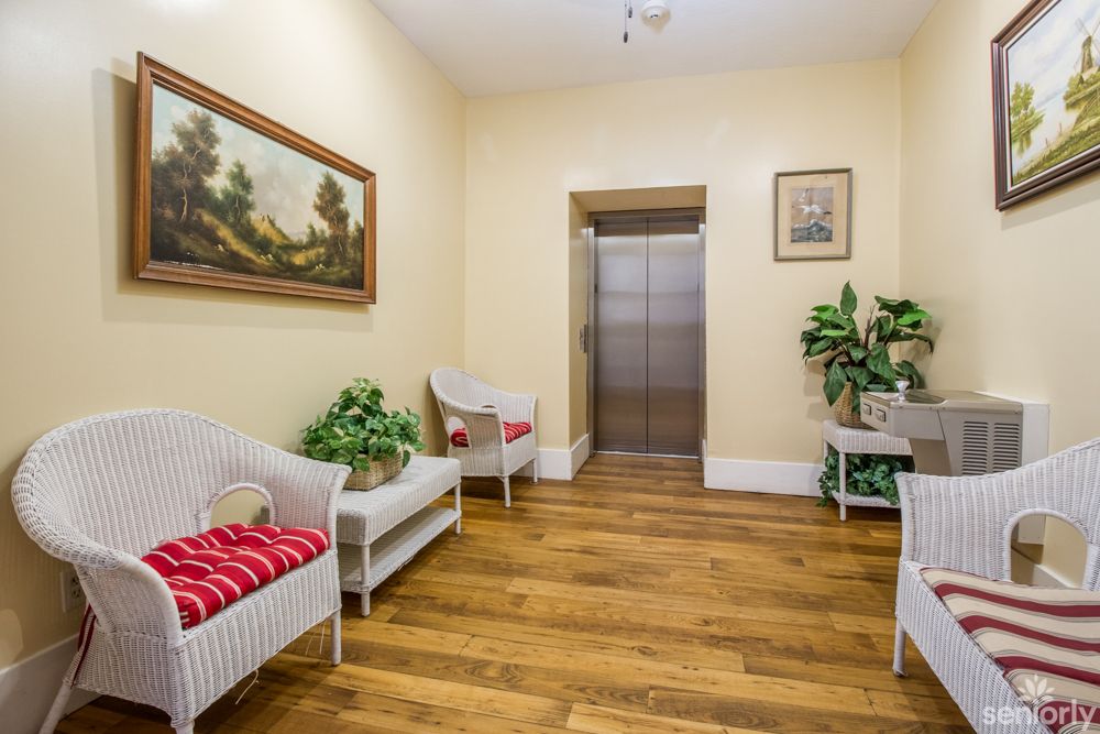 A cozy hallway with an elevator, featuring comfortable seating, plants, and artwork on the walls.
