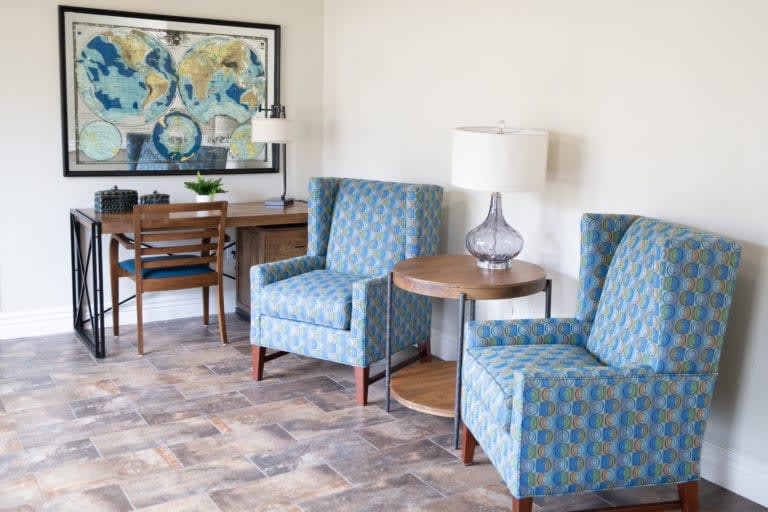 A cozy living room with two upholstered chairs, a table with a lamp, and artwork on the wall.