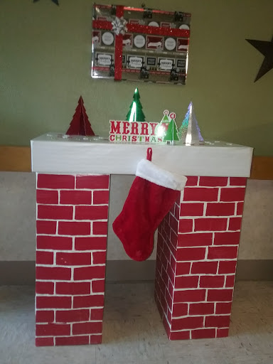 A cheerful Christmas decoration featuring a brick-style mantel with a festive stocking and colorful trees.