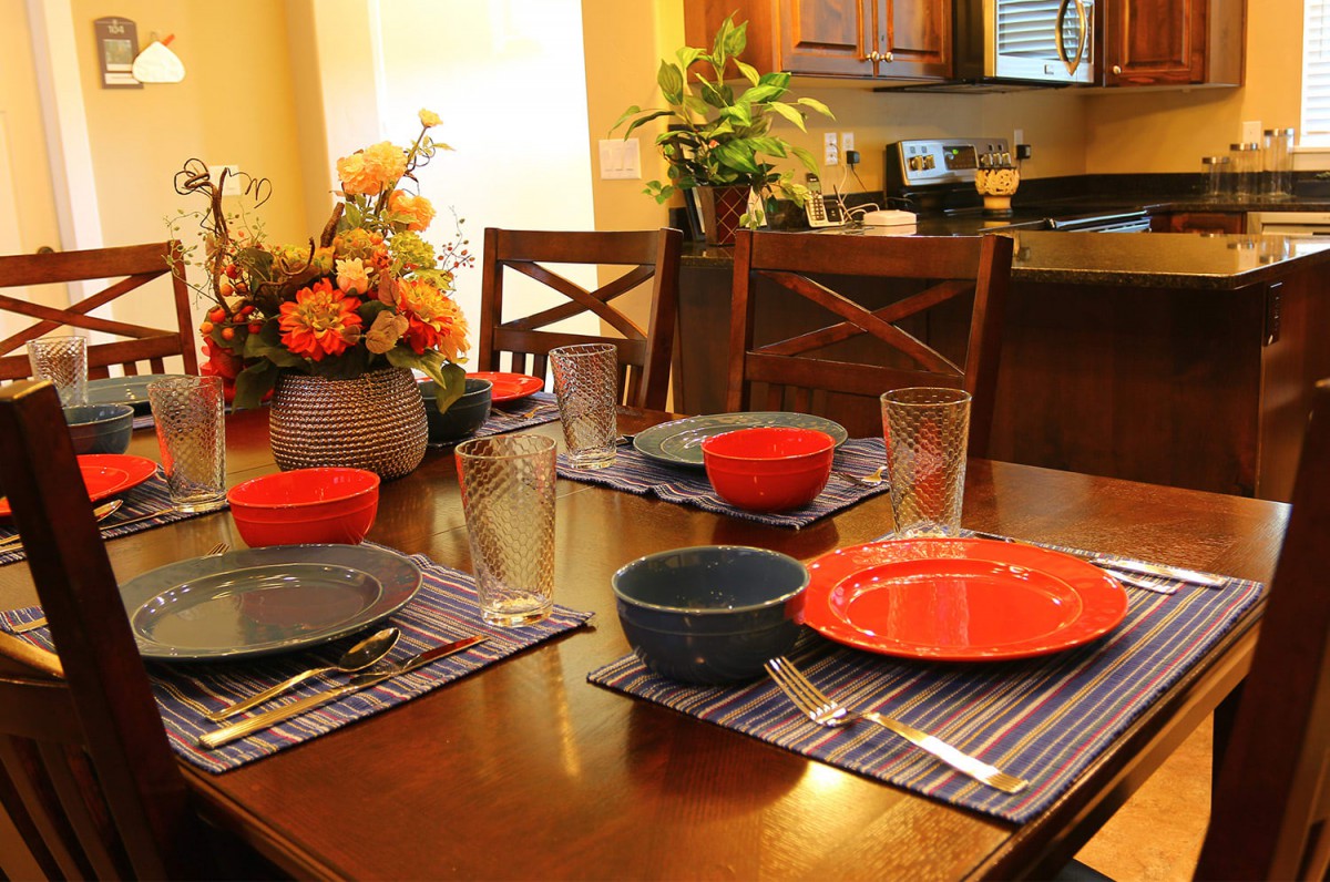 A dining table set with colorful plates, bowls, and glasses, decorated with a floral centerpiece.