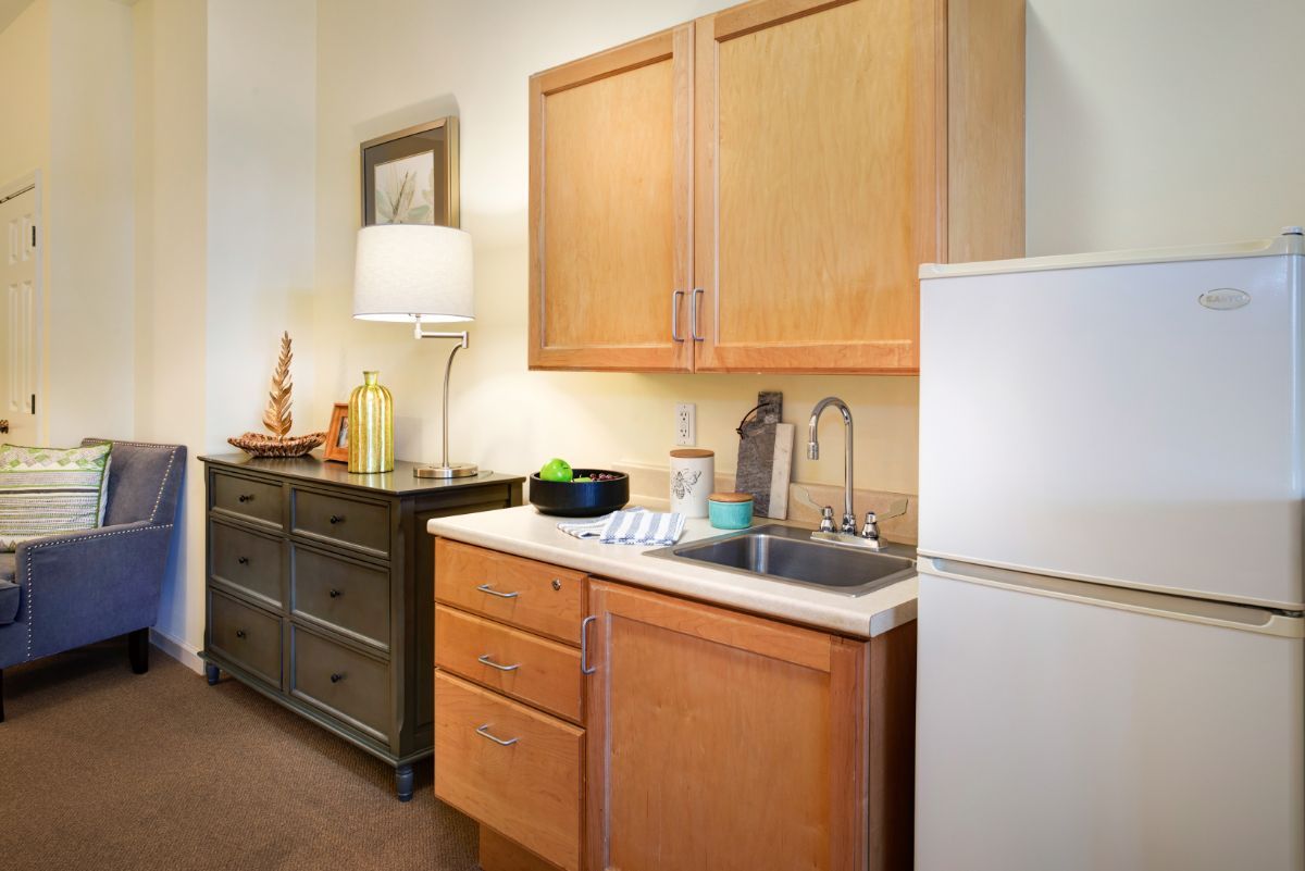 A compact kitchen area with wooden cabinets, a sink, refrigerator, and stylish decor.