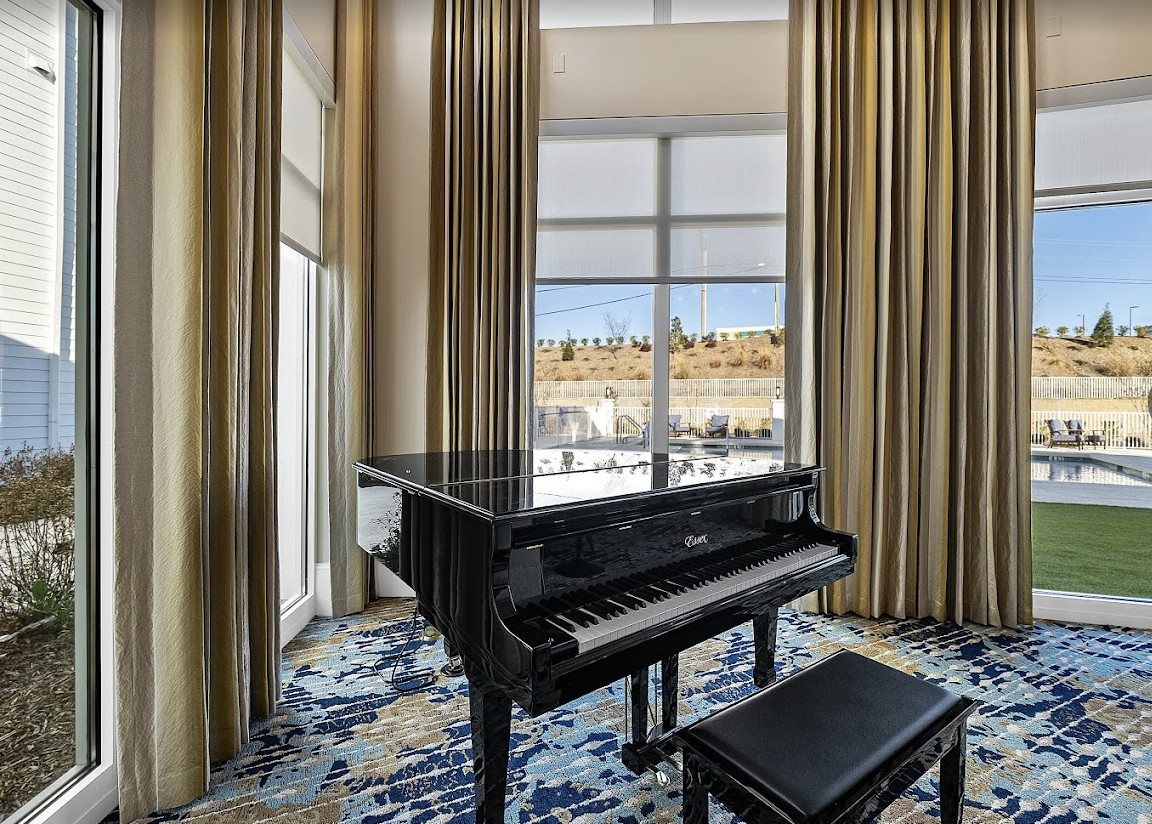 A grand piano positioned in a well-lit room with large windows and elegant curtains.